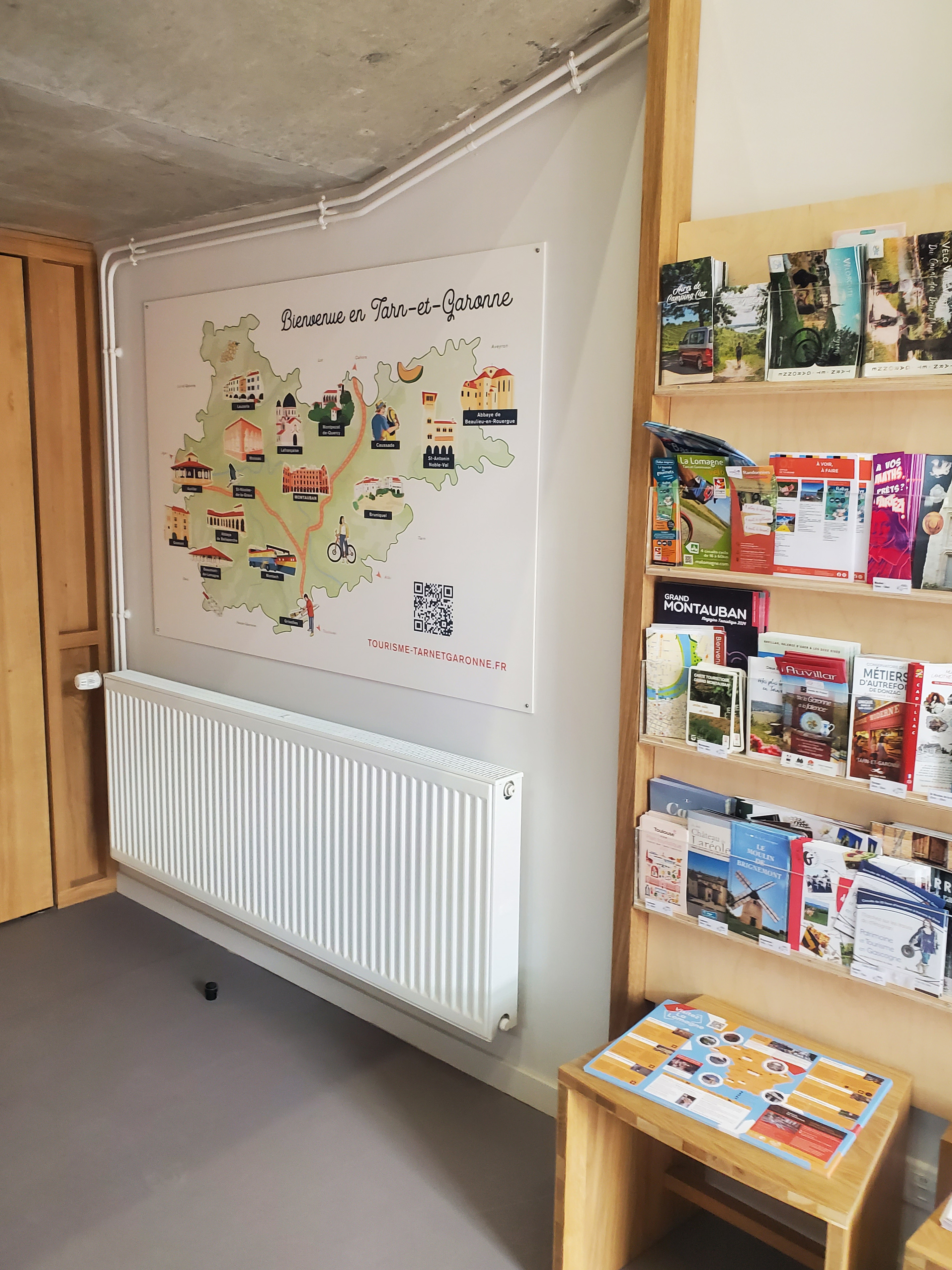 Carte du département posé sur un mur dans un office de tourisme avec différentes brochures autour