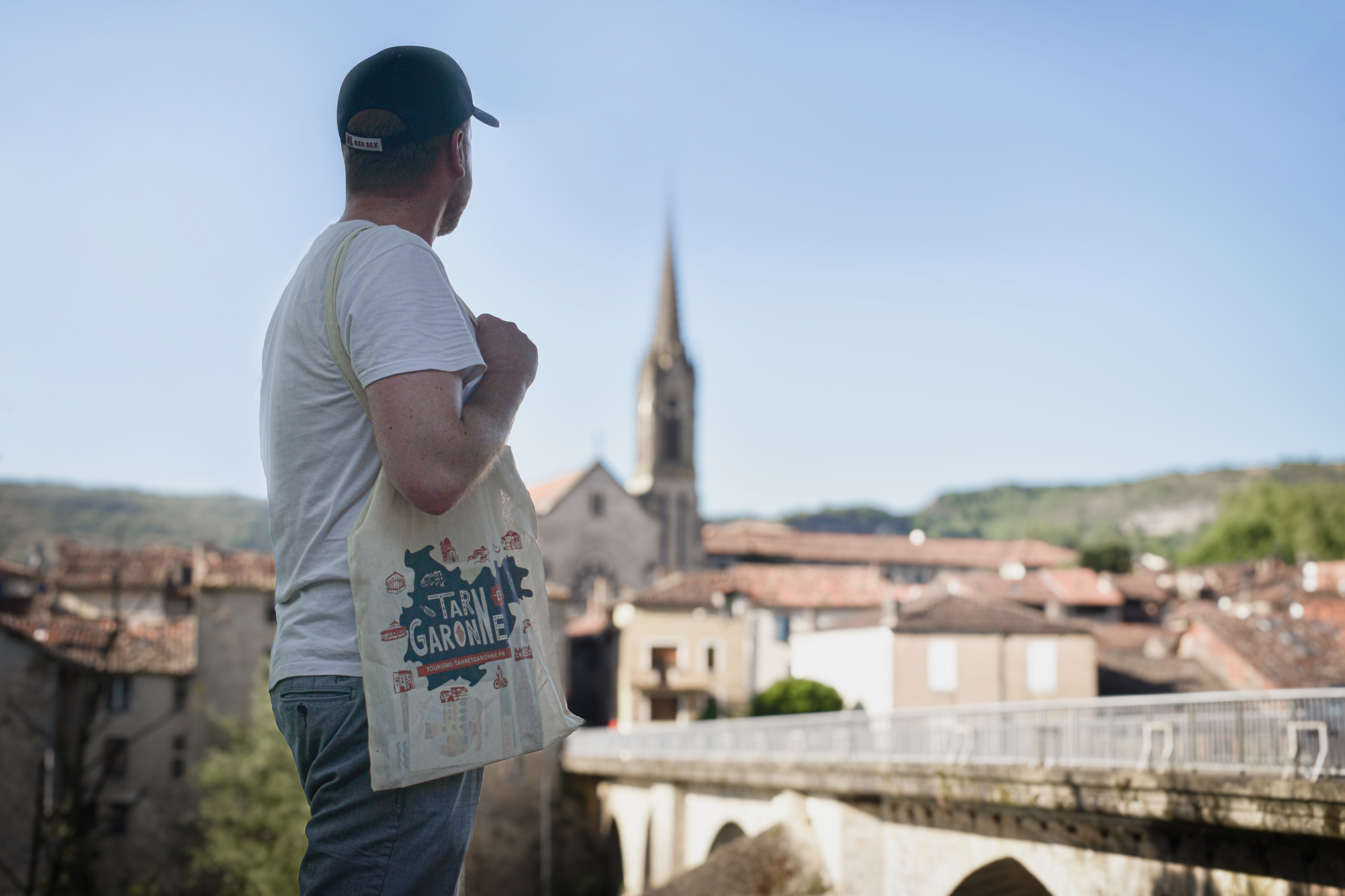 Un touriste observe les paysages de Saint-Antonin-Noble-Val, en portant un tot-bag touristique