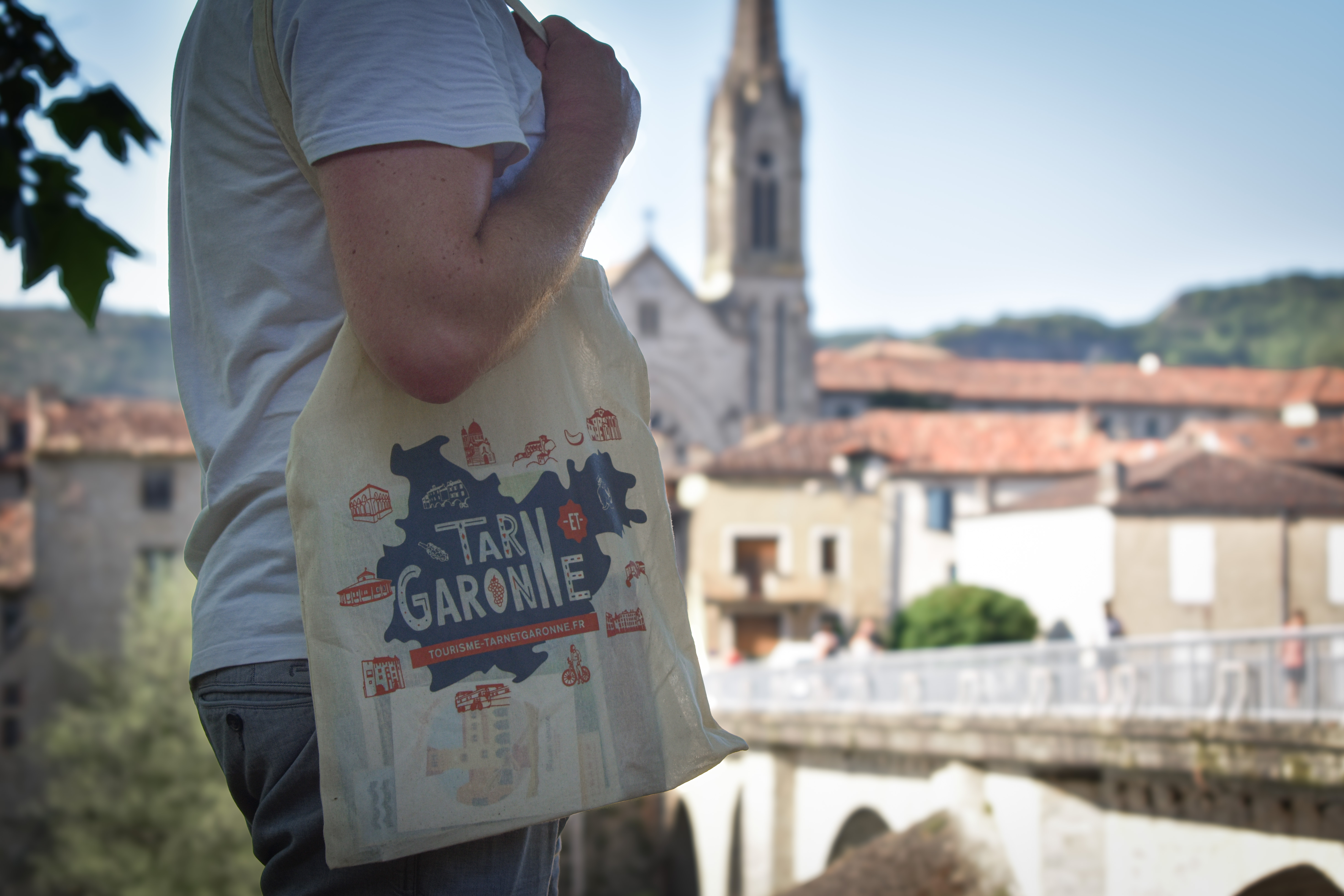 Zoom sur un tote-bag illustré valorisant le département avec en arrière-plan une commune française du Tarn-et-Garonne